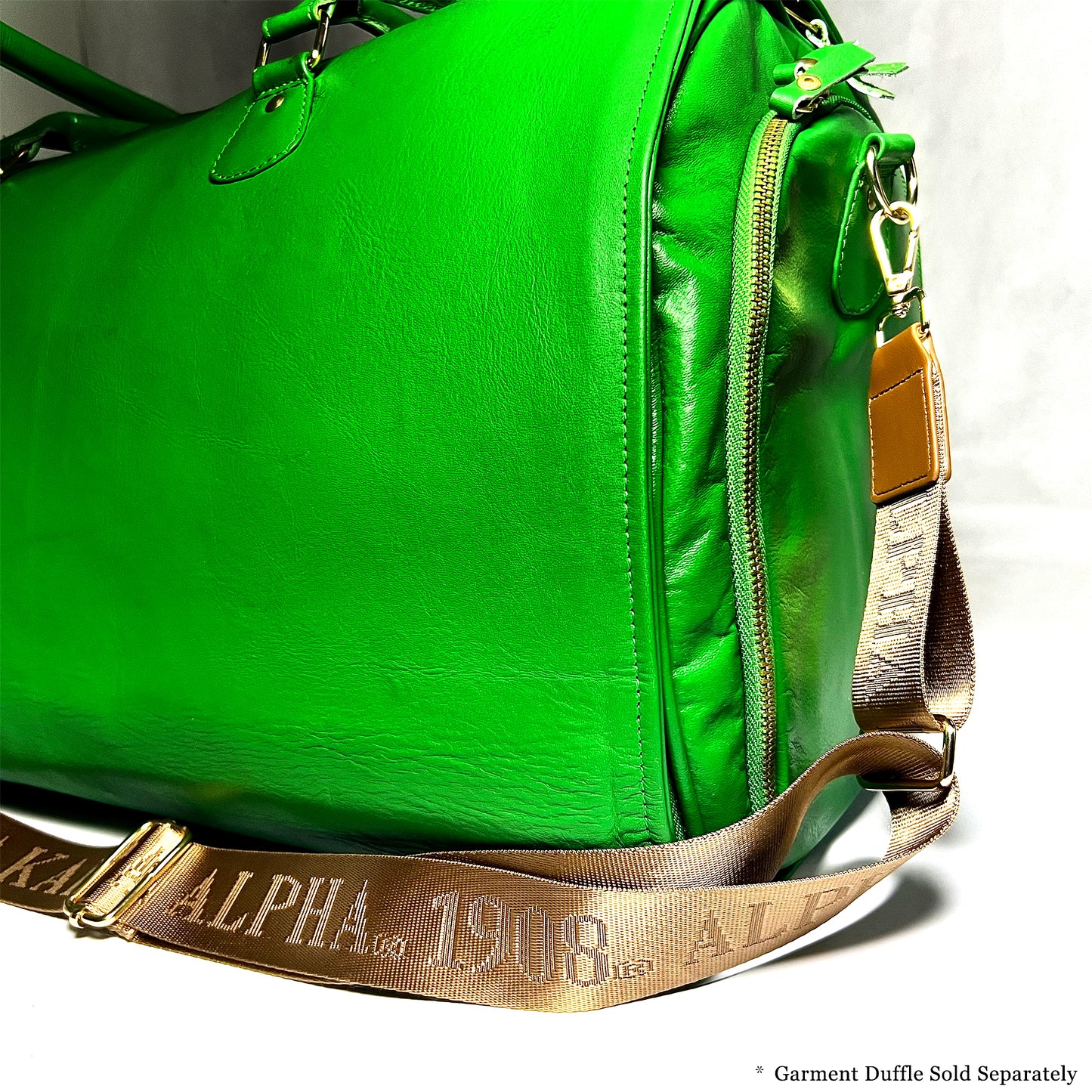 Bronze/Gold bag strap with debossed 'Alpha Kappa Alpha 1908' branding featured on a green leather duffle bag. Notice: Garment Duffle Sold Separately