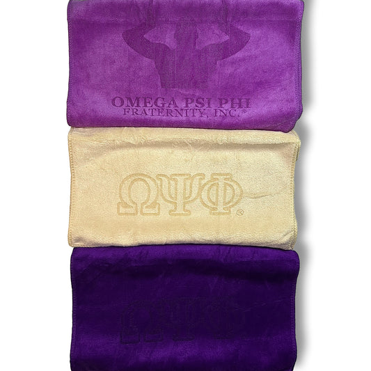 Purple and Old Gold colored towels with Omega Psi Phi fraternity logos on a white background