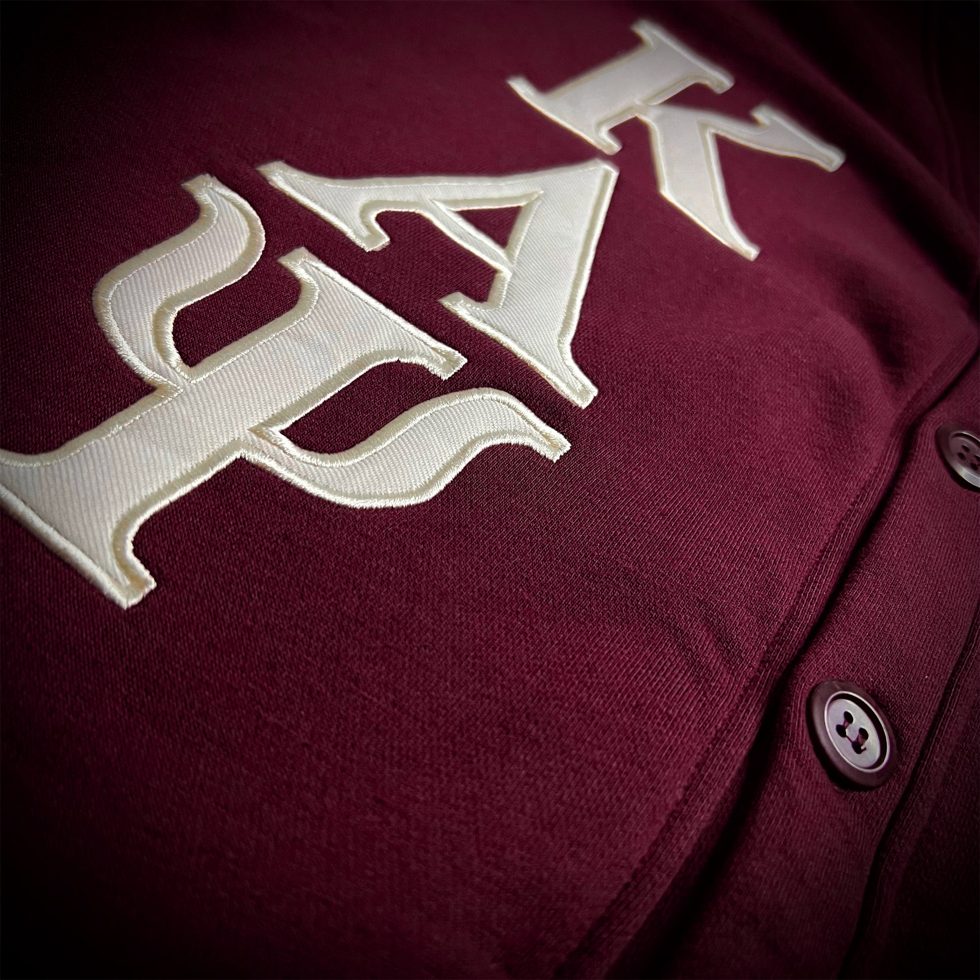 Close-up of a crimson button-front cardigan with large cream embroidered Greek letters across the chest.