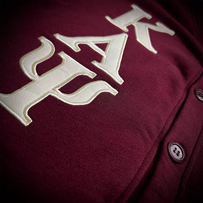 Close-up of a crimson button-front cardigan with large cream embroidered Greek letters across the chest.
