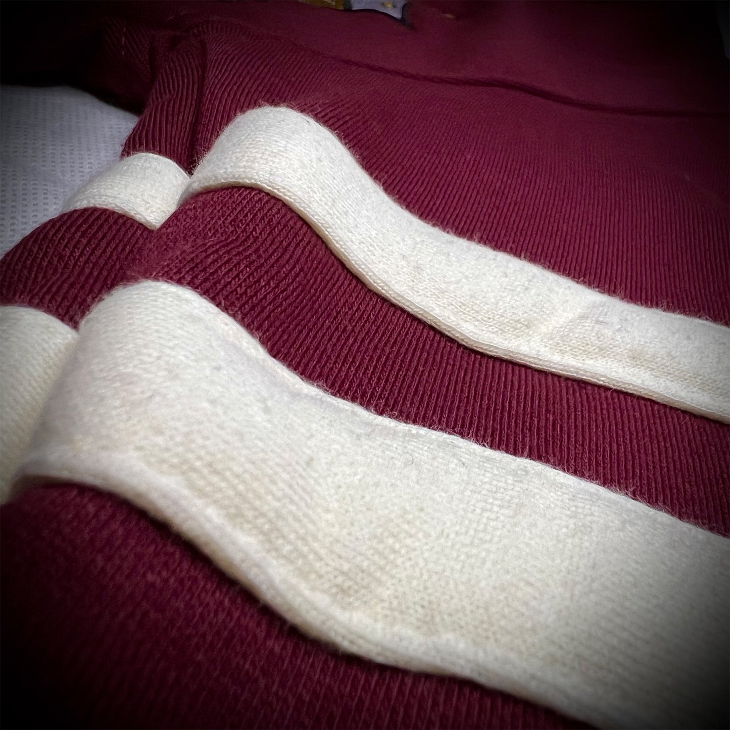 A close-up of a ribbed fleece sweater featuring thick horizontal cream-colored stripes over a deep crimson base.