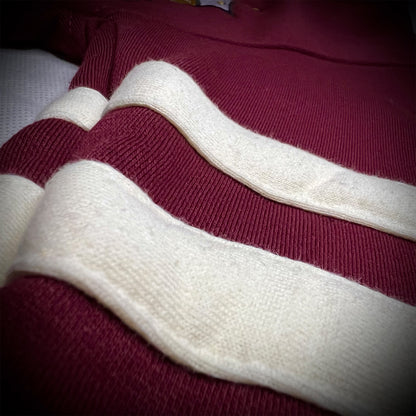 A close-up of a ribbed fleece sweater featuring thick horizontal cream-colored stripes over a deep crimson base.