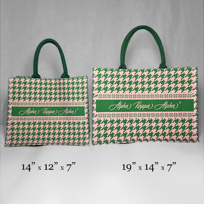 Two tote bags with green and pink houndstooth pattern and 'Alpha Kappa Alpha' text showing the size comparison. The left bag is the smaller version at 14 inches by 12 inches by 7 inches.  The right bag is the larger version at 19 inches by 14 inches by 7 inches.