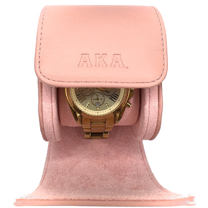 Pink watch holder with a gold watch inside, featuring the brand 'AKA'.